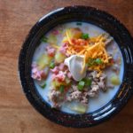 Overhead view of Loaded potato soup with ham, bacon, sausage, cheddar cheese and sour cream in a black bowl from www.ApronFreeCooking.com