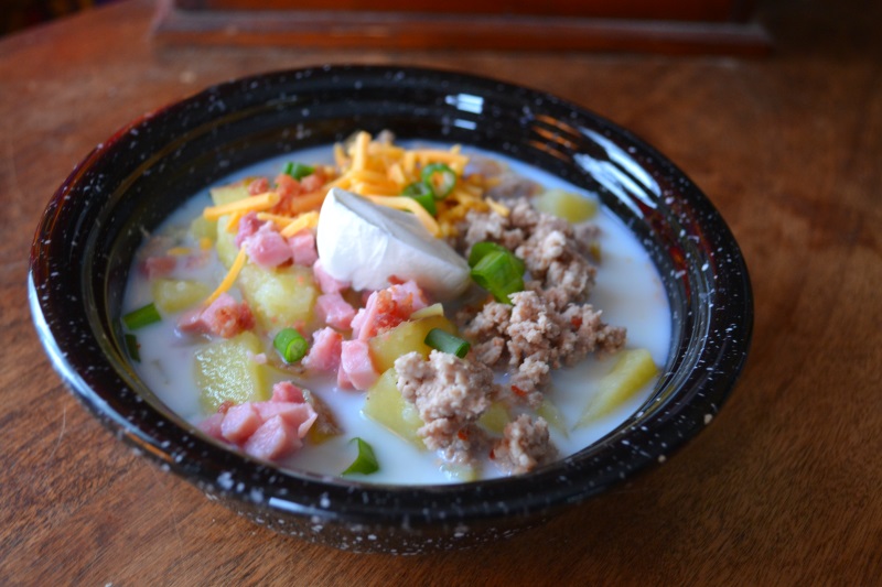 Loaded potato soup with ham, bacon, sausage, cheddar cheese and sour cream in a black bowl from www.ApronFreeCooking.com