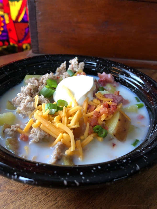 Close up view of Loaded potato soup with ham, bacon, sausage, cheddar cheese and sour cream in a black bowl from www.ApronFreeCooking.com