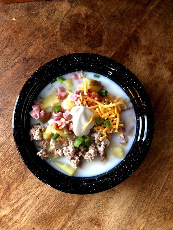 Overhead view of Loaded potato soup with ham, bacon, sausage, cheddar cheese and sour cream in a black bowl from www.ApronFreeCooking.com