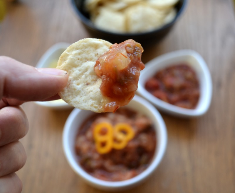 Pineapple Salsa on a chip with serving bowls in background.