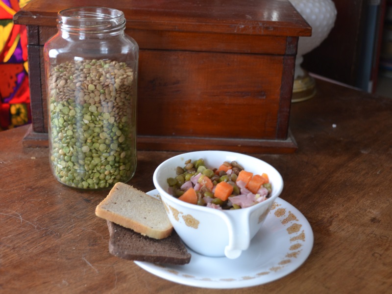 Split pea soup in white cup on a saucer with dried peas in background from www.ApronFreeCooking.com