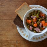 Overhead view of split pea soup with ham and carrots in tea cup on a white saucer from www.ApronFreeCooking.com