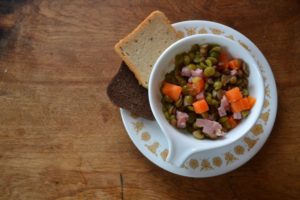 Overhead view of split pea soup with ham and carrots in tea cup on a white saucer from www.ApronFreeCooking.com