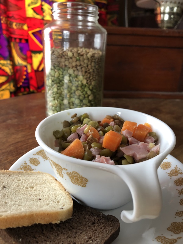 close up of Split pea soup in white cup on a saucer with dried peas in background from www.ApronFreeCooking.com