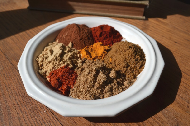 Red, orange, tan, and brown spices piled on a while plate to make up Moroccan Spice Mix from www.ApronFreeCooking.com