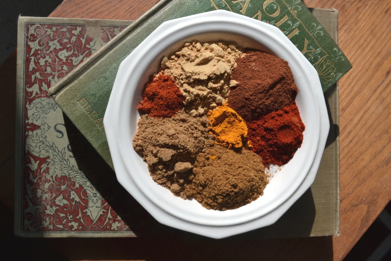 Overhead view of white plate with brown, orange and red individual spices used to make Moroccan Spice Mix from www.ApronFreeCooking.com
