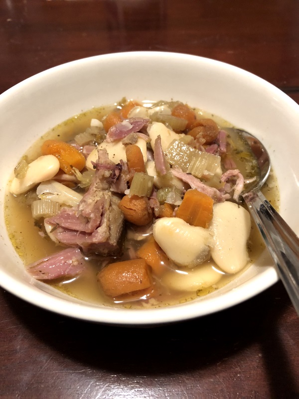 White bowl of bean and ham soup make with carrots and celery