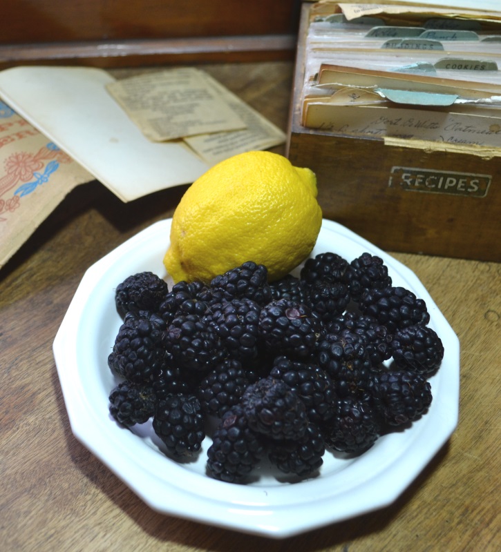 Lemon and black raspberries on a white plate.