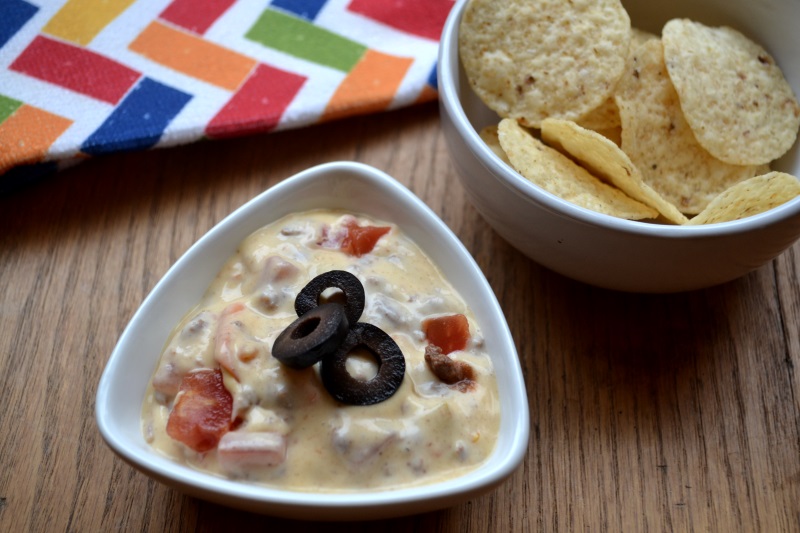 Simple Queso Dip with nacho chips in a white bowl from www.ApronFreeCooking.com