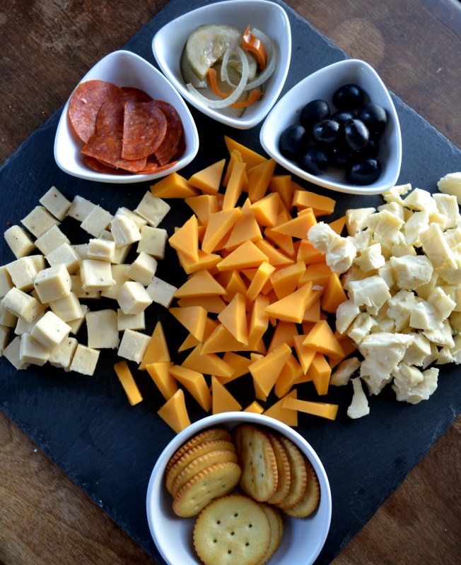 Meat and Cheese Board with three kinds of cheese on gray slate and using white bowls for olives and crackers. from www.ApronFreeCooking.com