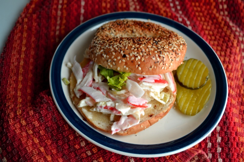Easy Crab Salad Sandwich recipe served on a bagel with red white and blue background from www.ApronFreeCooking.com