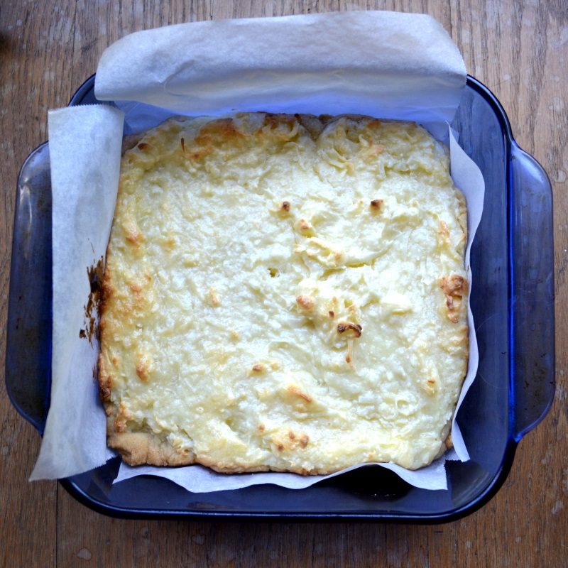 Coconut Cream Cheesecake in blue baking dish with parchment paper hanging over edge from www.ApronFreeCooking.com