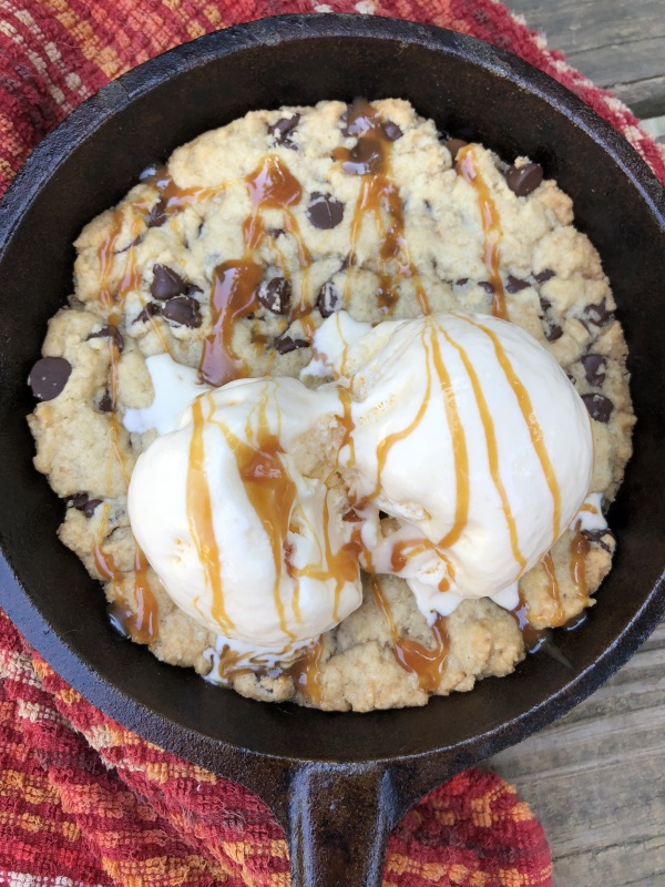 Overhead view of Chocolate Chip Skillet Cookie served with vanilla ice cream and caramel sauce in cast iron skillet from www.ApronFreeCooking.com