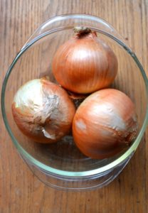 Three onions in brown skins in a clear glass bowl on wooden background from www.ApronFreeCooking.com