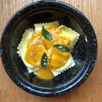 Pumpkin sauce with sage leaves in brown butter over cheese ravioli served in a black bowl from www.ApronFreeCooking.com