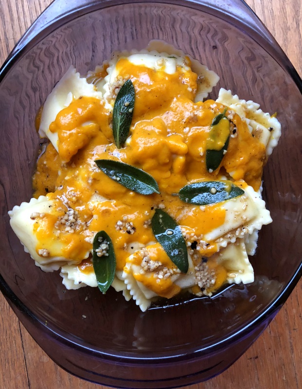 Pumpkin sauce with sage leaves in brown butter over cheese ravioli in a purple serving dish from www.ApronFreeCooking.com