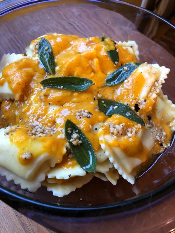 Pumpkin sauce with sage leaves in brown butter over cheese ravioli in a purple serving dish from www.ApronFreeCooking.com
