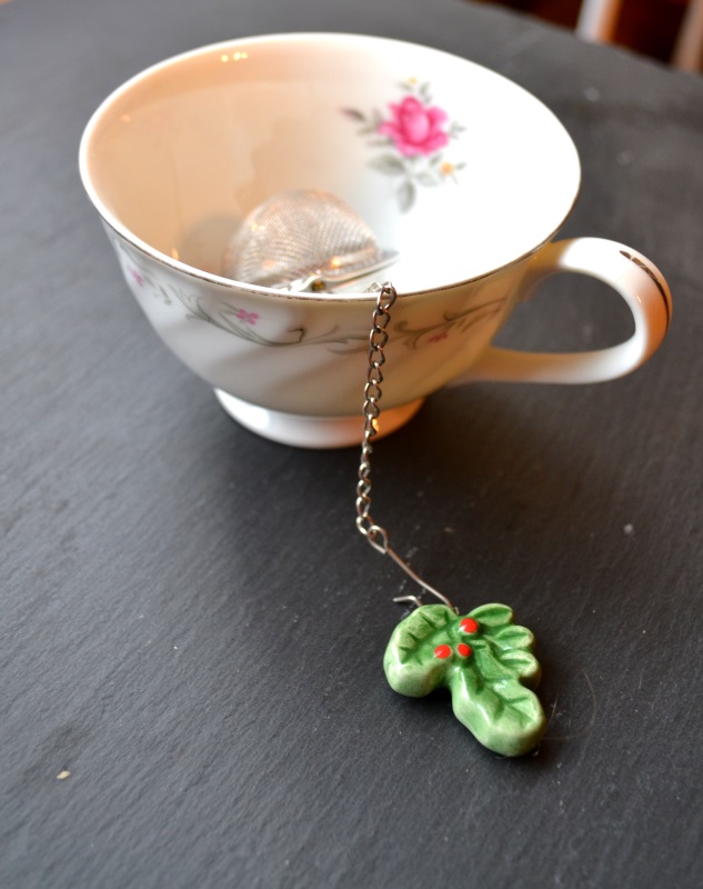 Pretty white tea cup with red rose and tea strainer with green leaf from www.ApronFreeCooking.com