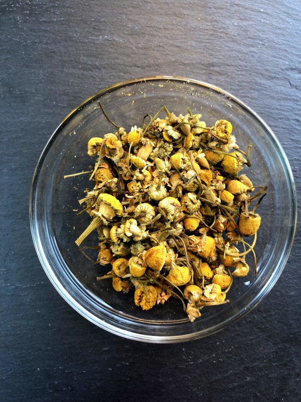 Yellow chamomile flowers in glass bowl on gray background from www.ApronFreeCooking.com