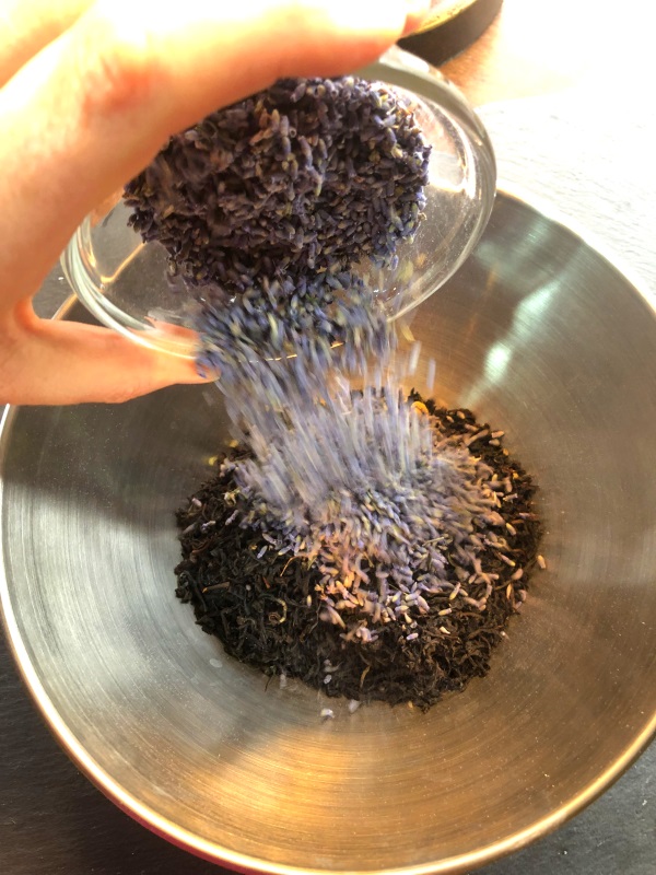 Lavender flower buds being added to bowl of loose leaf tea blend from www.ApronFreeCooking.com