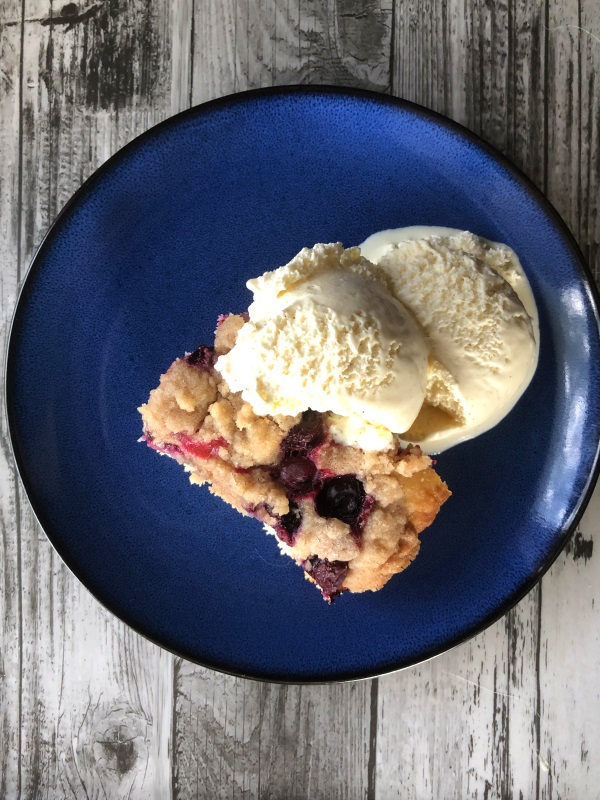 Vintage recipe for blueberry buckle served on a blue plate with scoop of vanilla ice cream. 