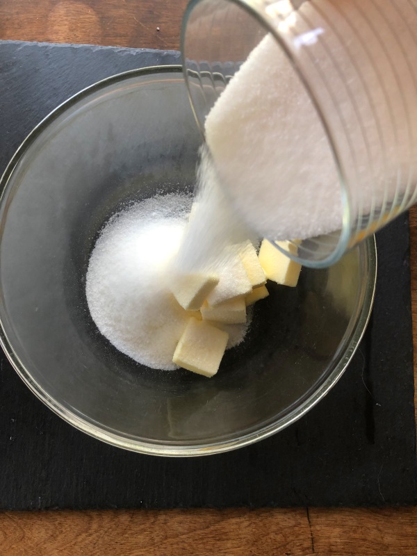 Sugar poured into bowl on top of butter 