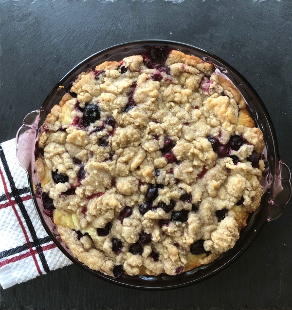 Blueberry Buckle with crumb topping in purple pie dish on white towel. 