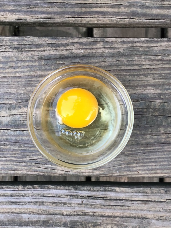 Overhead view of Blueberry Cornbread Muffin Ingredients Egg in a small glass bowl on wooden background.