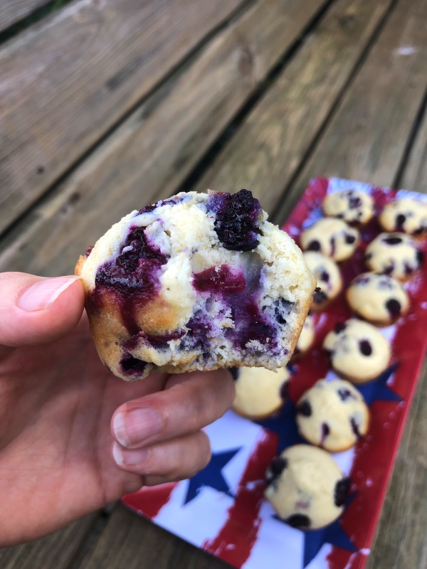 Blueberry Cornbread Muffins on a flag printed tray in background. Forefront is a blueberry cornbread muffin with a bite missing.