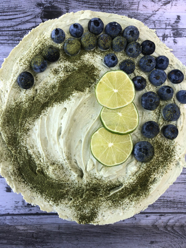Matcha no bake cheesecake with blueberries, lime slices and matcha powder topping over head view
