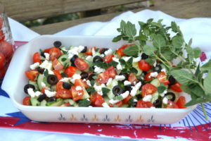 white dish filled with greek salad, tomatoes, black olives, cucumber, feta cheese and sprigs of fresh oregano