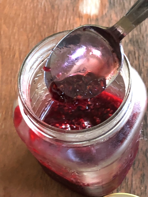 spoon placing homemade raspberry syrup in mason jar